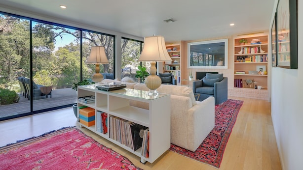 A modern living room with a glass coffee table, a white sofa, a blue armchair, and a bookshelf filled with books and decorative items. - Modern Austin Home w/ Yard ~ 1 Mi From Acl! (Austin)