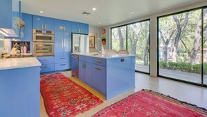 A modern kitchen with blue cabinets, stainless steel appliances, and a large window offering a view of trees. - Modern Austin Home w/ Yard ~ 1 Mi From Acl! (Austin)