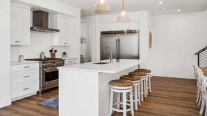 Een moderne keuken met witte kasten, roestvrijstalen apparatuur en een centraal eiland met barkrukken.