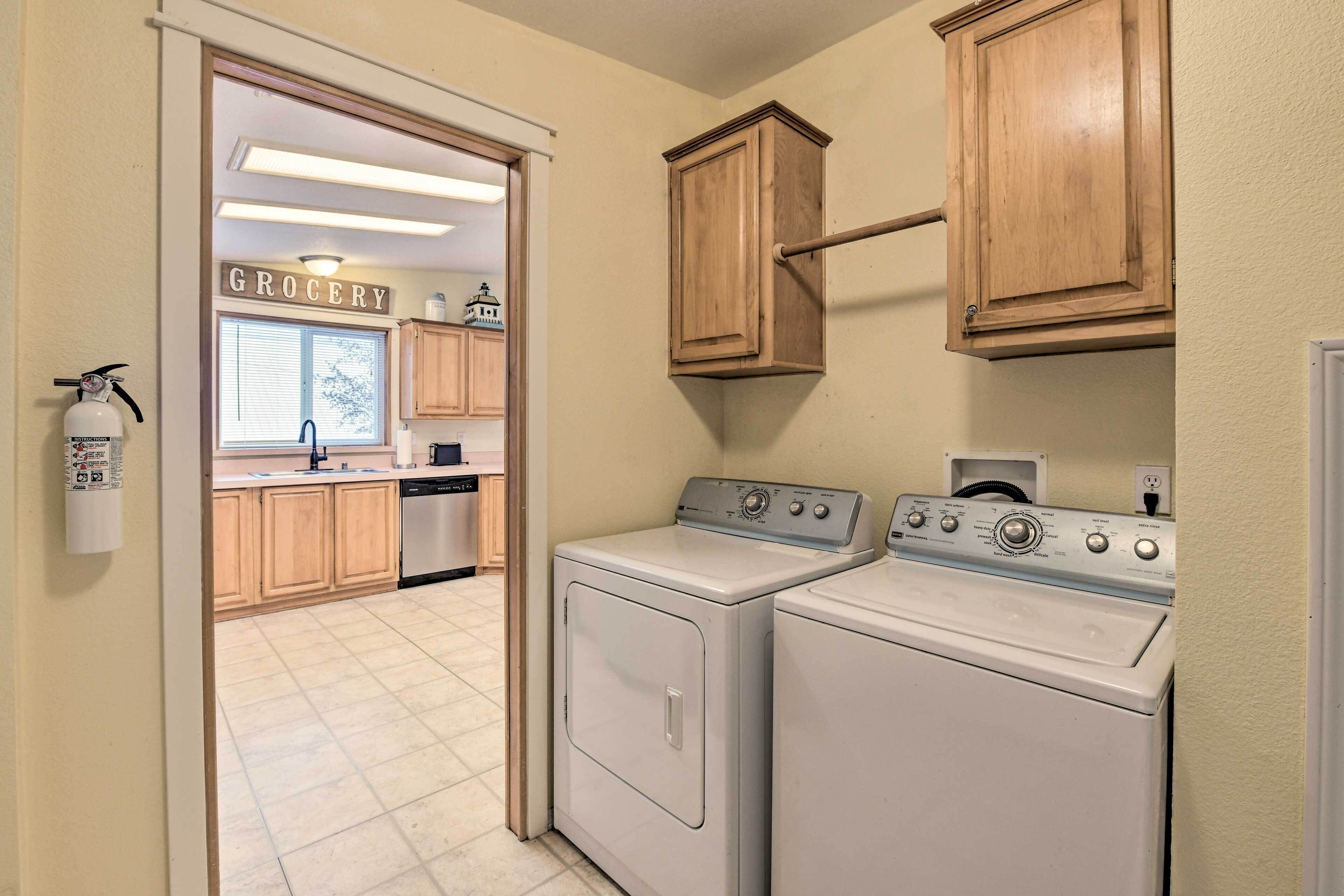A laundry room with two front-loading washers and dryers, wooden cabinets, a fire extinguisher, and a sign indicating the room is for the grocery area.