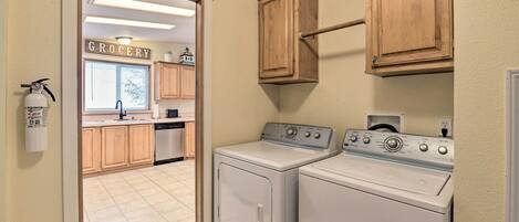 A laundry room with two front-loading washers and dryers, wooden cabinets, a fire extinguisher, and a sign indicating the room is for the grocery area.