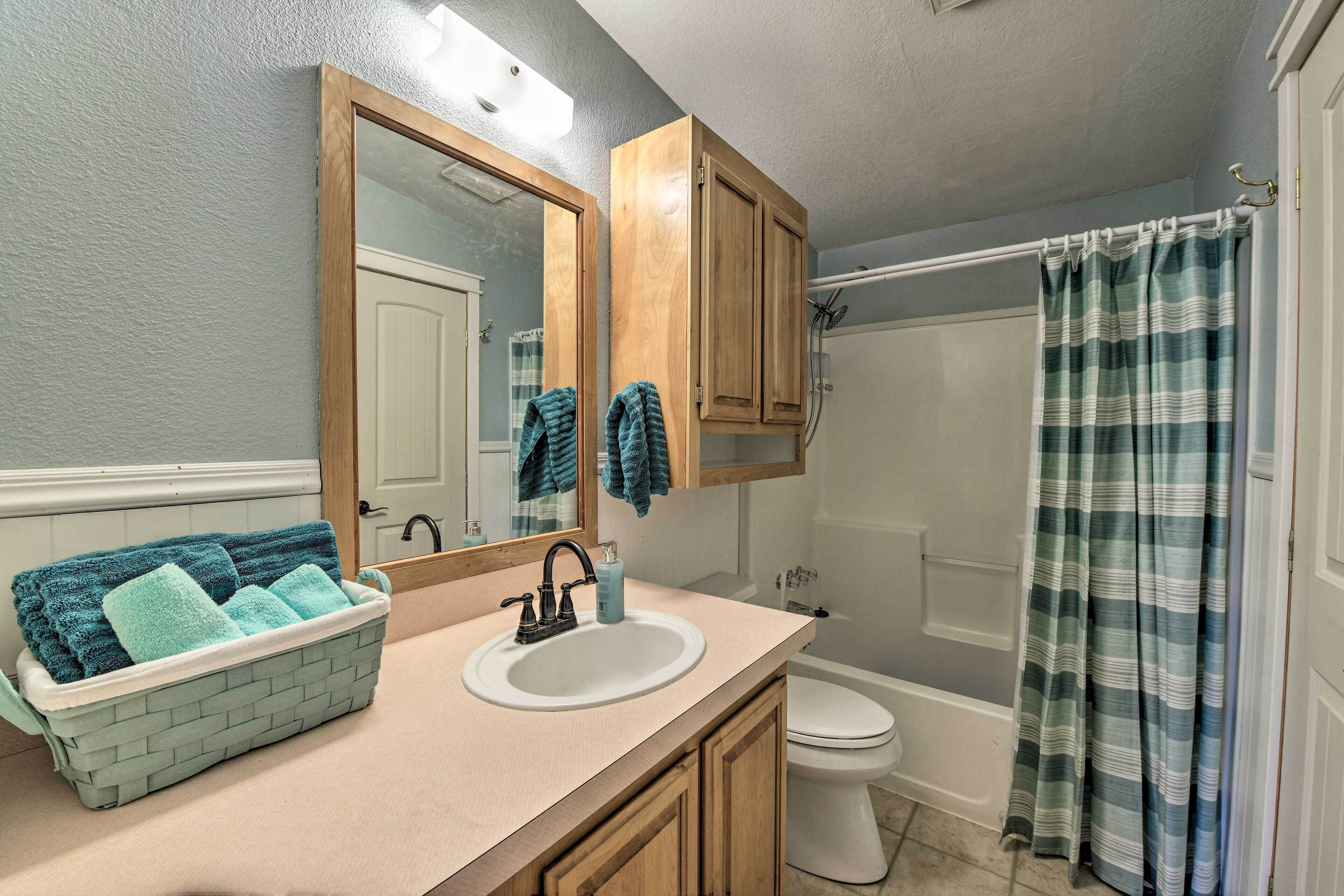 Une salle de bain avec un lavabo blanc, des meubles en bois, un miroir, un porte-serviettes, un rideau de douche et des toilettes.