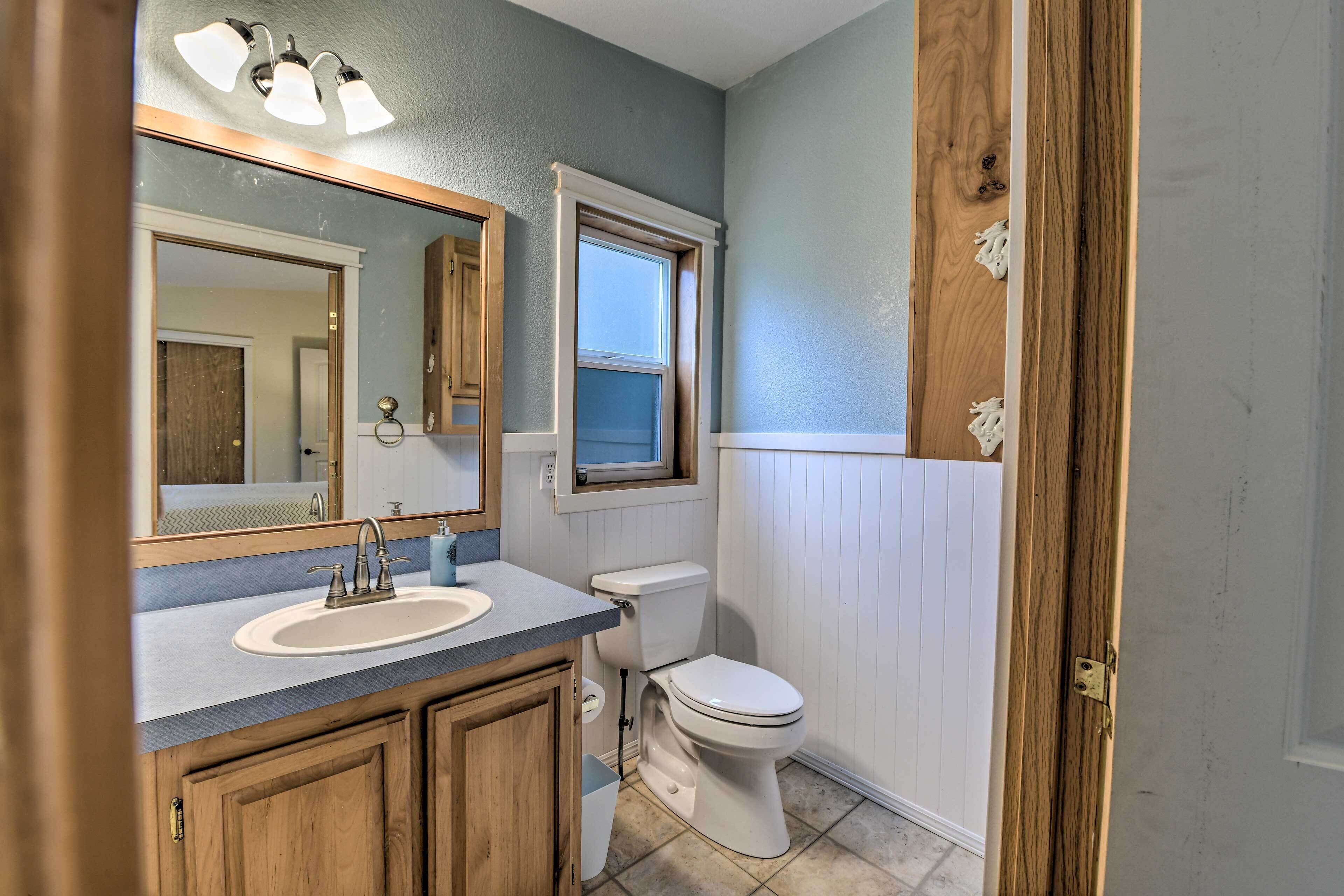 A bathroom with a sink, mirror, toilet, and window.