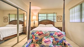 Une chambre à coucher comprenant un lit, une table de chevet, un miroir, une fenêtre avec des stores et une lampe fixée au mur.