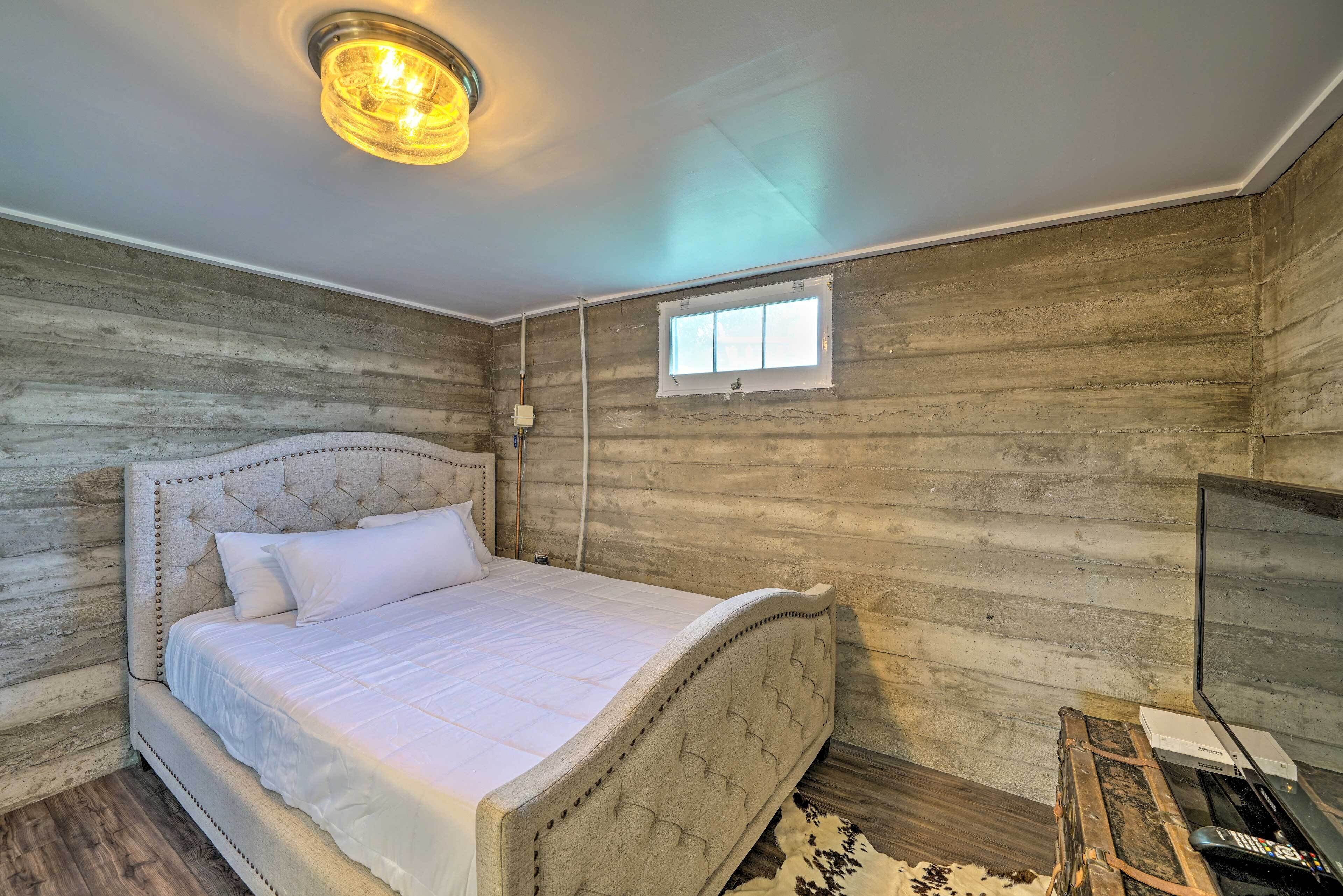 Um quarto com uma cama grande, uma parede de madeira, uma janela pequena e uma televisão sobre um suporte de madeira.