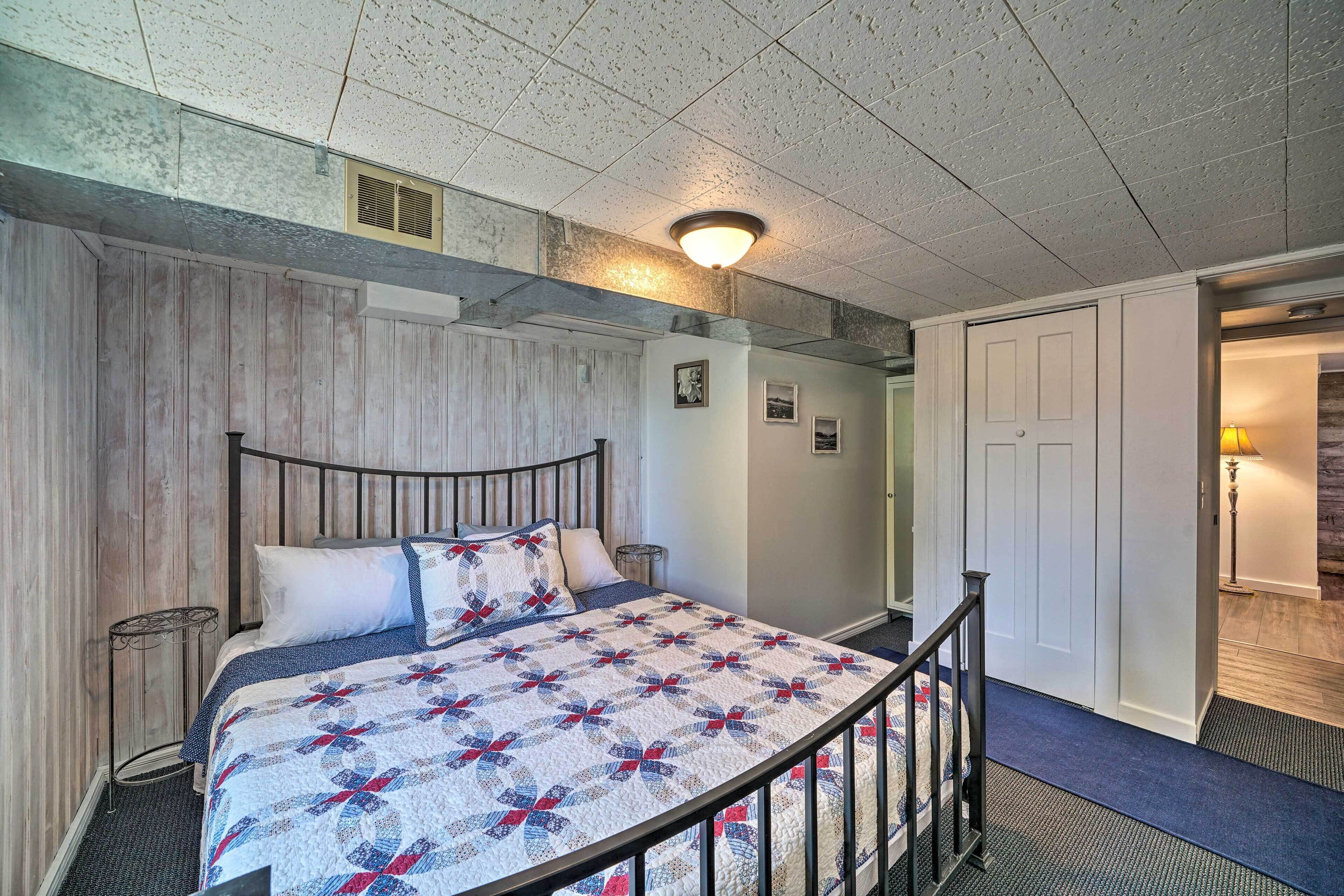 A bedroom with a wooden headboard, a quilted bedspread, a nightstand, and a wall-mounted lamp.