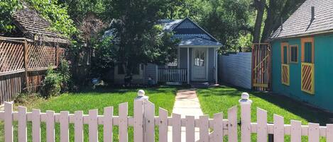 A residential property with a white picket fence, a pathway leading to a house with a blue roof, and a neighboring house with a yellow exterior.