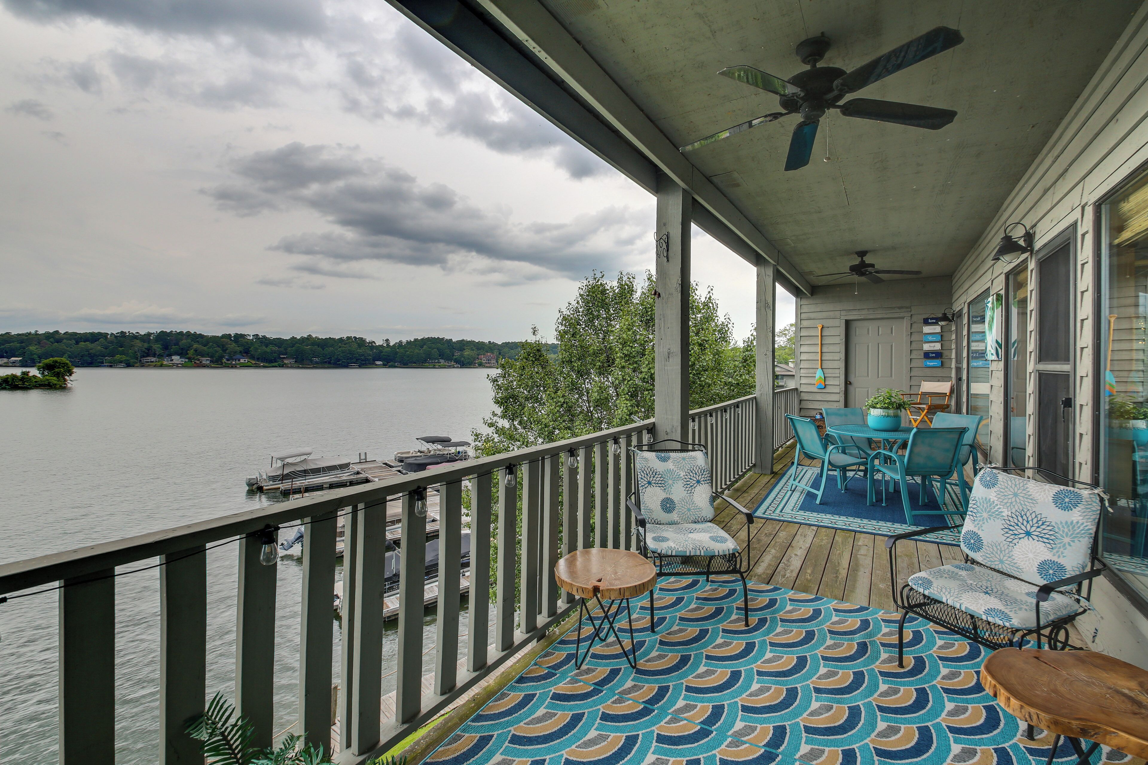 A covered deck with a view of a lake, outdoor furniture, and a ceiling fan.