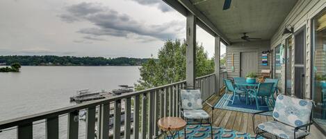 A covered deck with a view of a lake, outdoor furniture, and a ceiling fan.