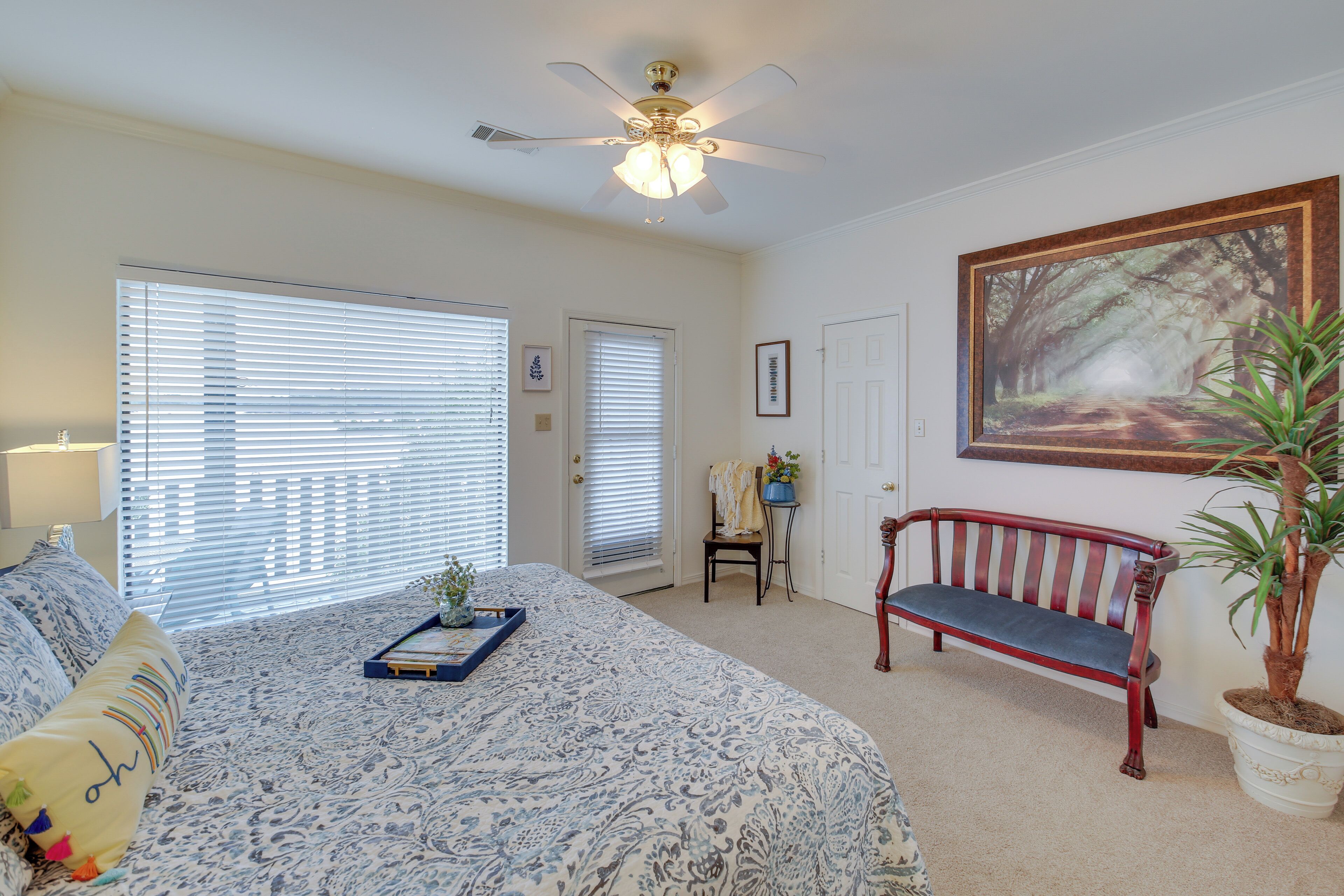 A bedroom with a large bed, a ceiling fan, a bench, and a potted plant.