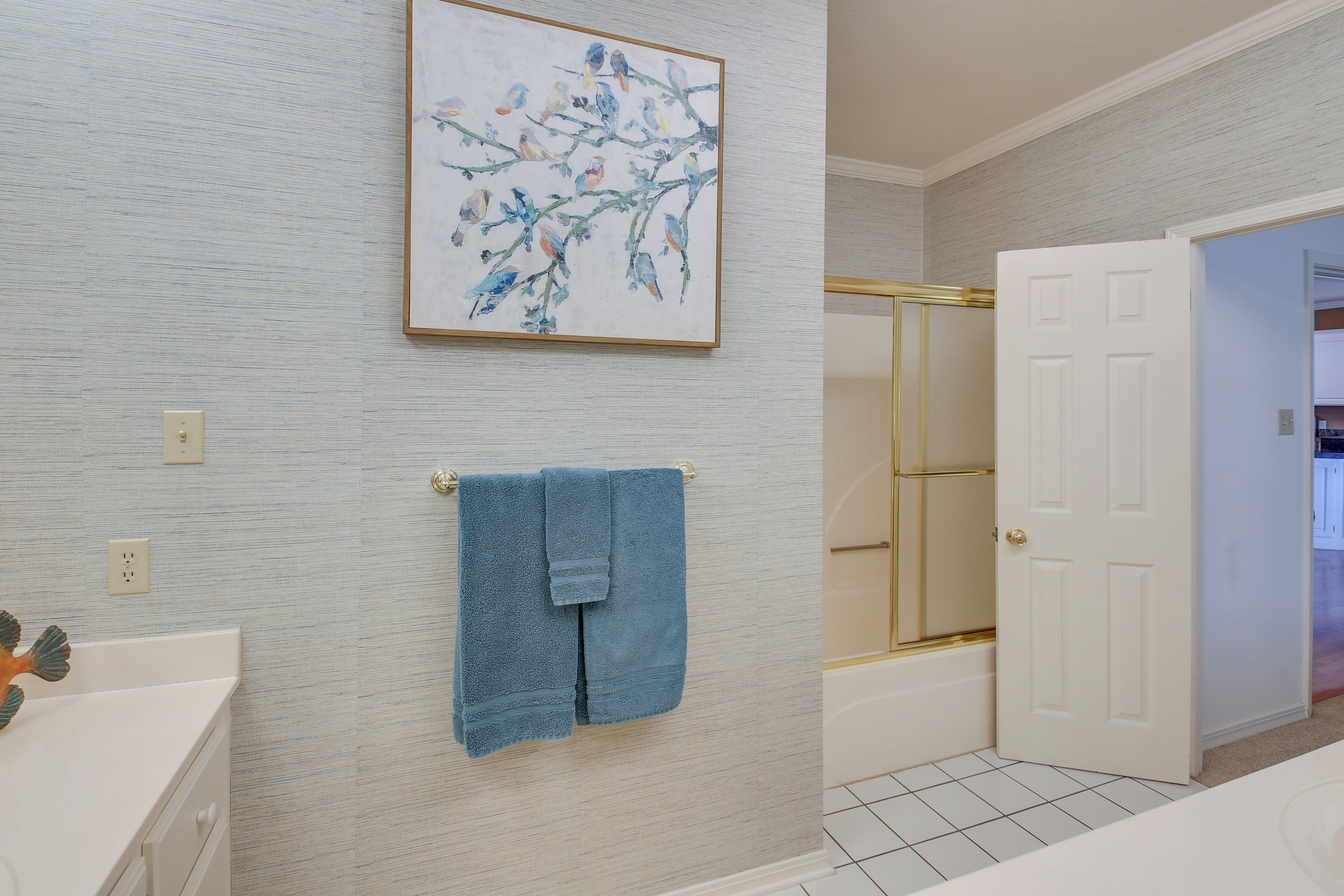 A bathroom with a white bathtub, a white door, and a blue towel hanging on the wall.