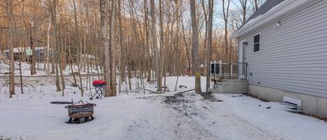 A snowy backyard with a grill, a fire pit, and a house.
