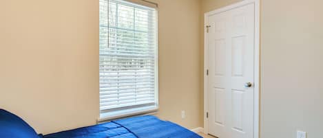 A bedroom with a bed, a window with blinds, and a door.