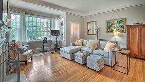 A spacious living room with a large window, a grey sectional sofa, a small table, and a wooden cabinet.