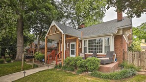 A house with a covered porch, a brick exterior, and a front yard with a lawn and shrubs.