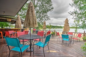 Une terrasse extérieure avec des tables et des chaises rondes, une plateforme en bois et une vue sur une étendue d’eau.