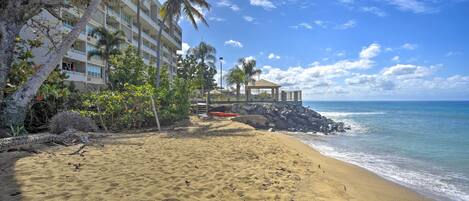 A beach with a building, palm trees, and a gazebo.