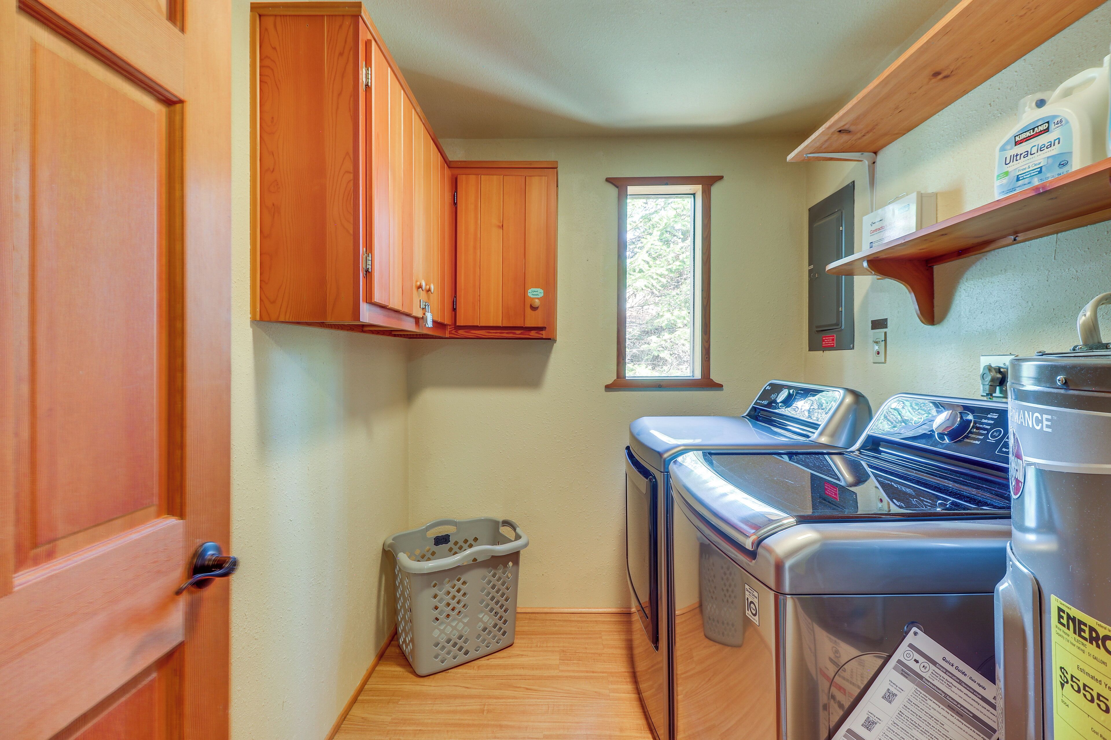 A laundry area with a washing machine, dryer, wooden cabinets, a window, and a laundry basket.