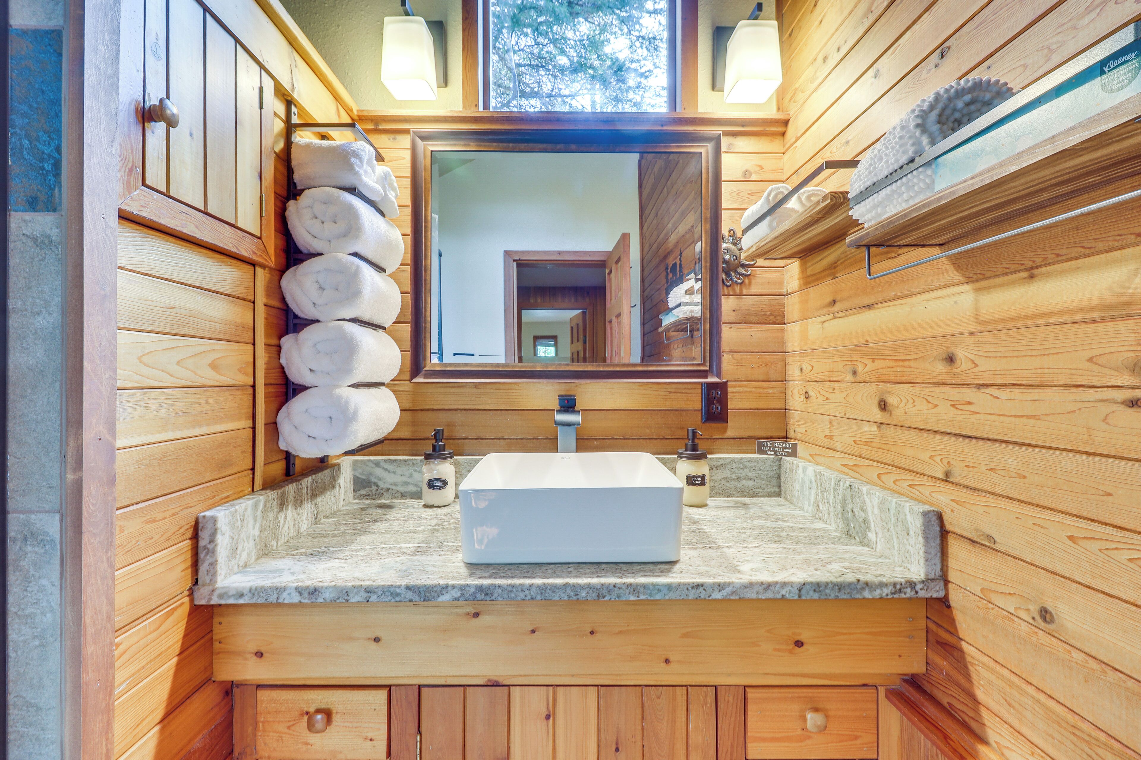 Un baño de cabaña de madera con encimera de piedra, un espejo grande y un perchero con toallas.