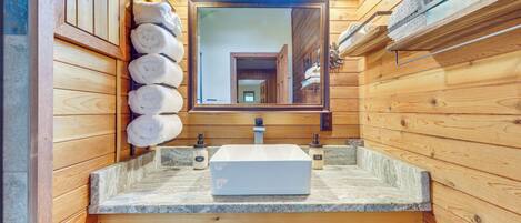 Un baño de cabaña de madera con encimera de piedra, un espejo grande y un perchero con toallas.