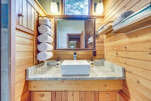 A wooden cabin bathroom with a stone countertop, a large mirror, and a towel rack with towels. - 'griz Den' Cabin w/ 2 King Beds Near Glacier! (Hungry Horse)