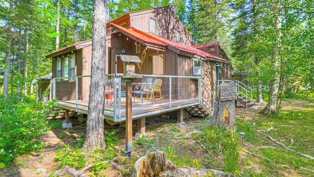 A wooden cabin with a deck, surrounded by trees. - 'griz Den' Cabin w/ 2 King Beds Near Glacier! (Hungry Horse)