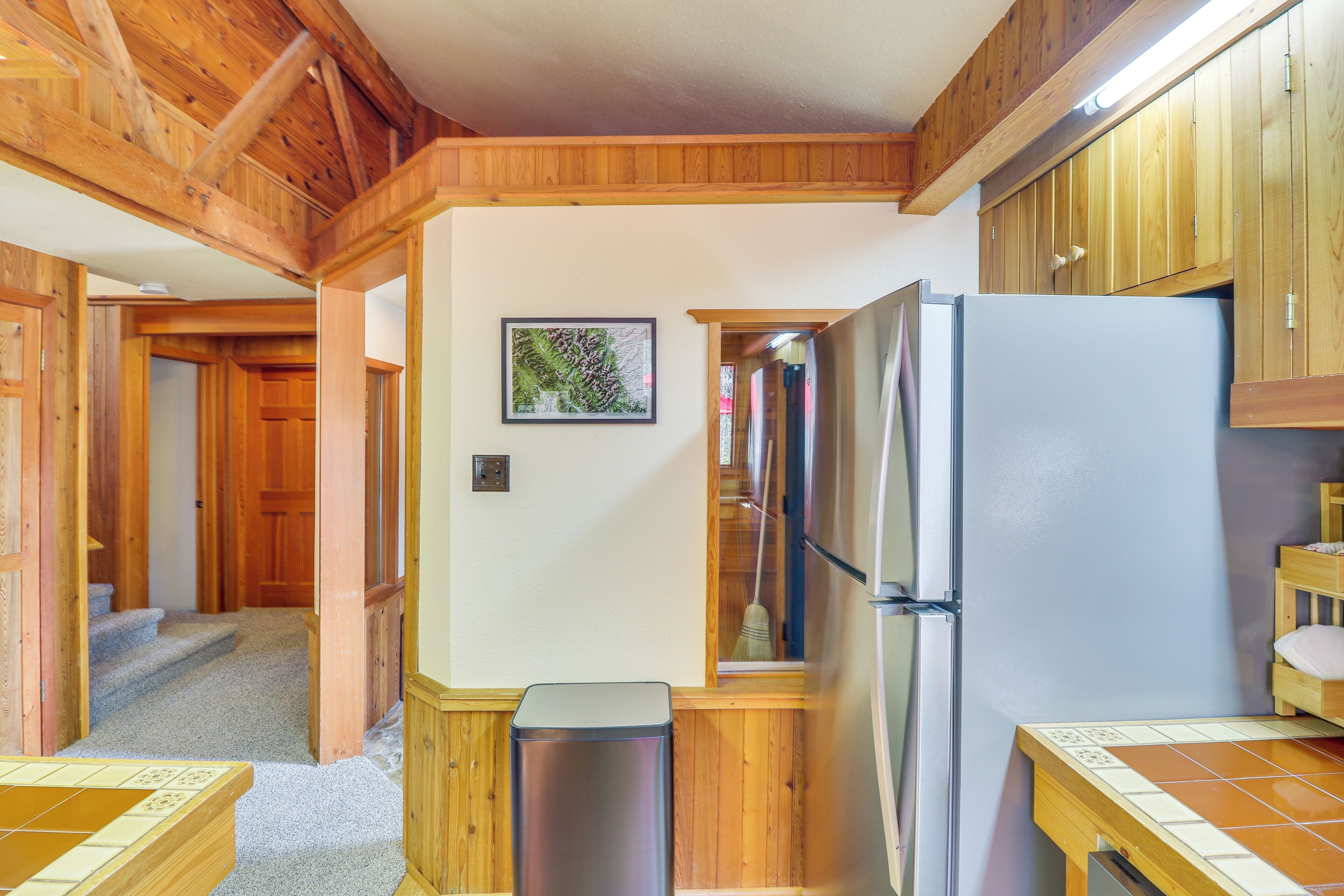 A kitchen with wooden cabinets, a refrigerator, and a trash bin.