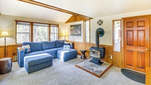 A cozy living room with a sectional sofa, a fireplace, and large windows. - 'griz Den' Cabin w/ 2 King Beds Near Glacier! (Hungry Horse)