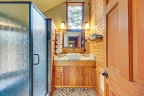 A wooden bathroom with a glass shower door, a sink with a mirror above, and a towel rack with towels. - 'griz Den' Cabin w/ 2 King Beds Near Glacier! (Hungry Horse)