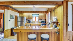 A kitchen with wooden cabinets, a stainless steel refrigerator, a microwave, and a wooden island with two stools. - 'griz Den' Cabin w/ 2 King Beds Near Glacier! (Hungry Horse)