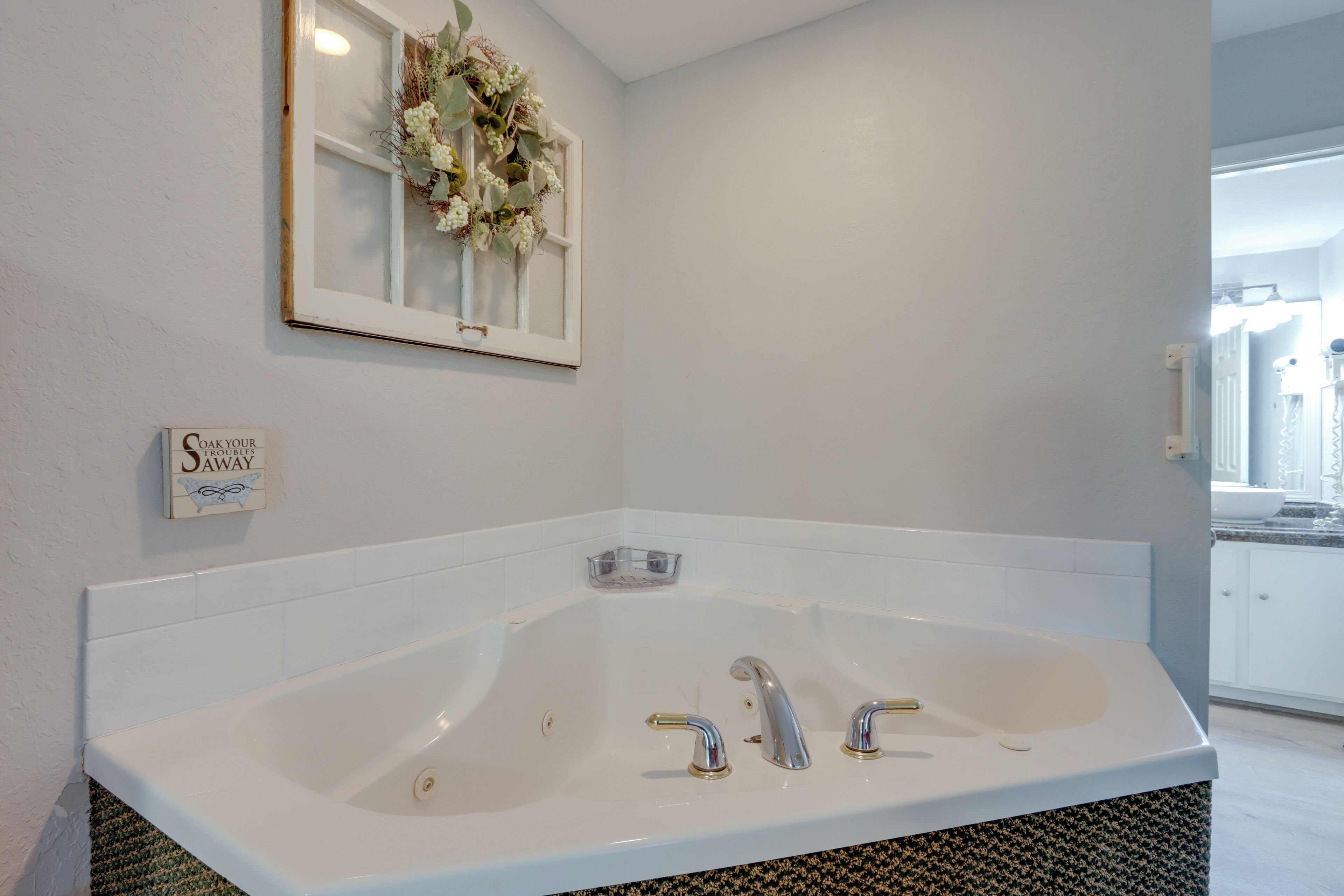 A modern bathroom with a large bathtub, a framed window with a floral wreath, and a sign on the wall.