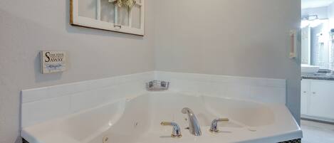 A modern bathroom with a large bathtub, a framed window with a floral wreath, and a sign on the wall.