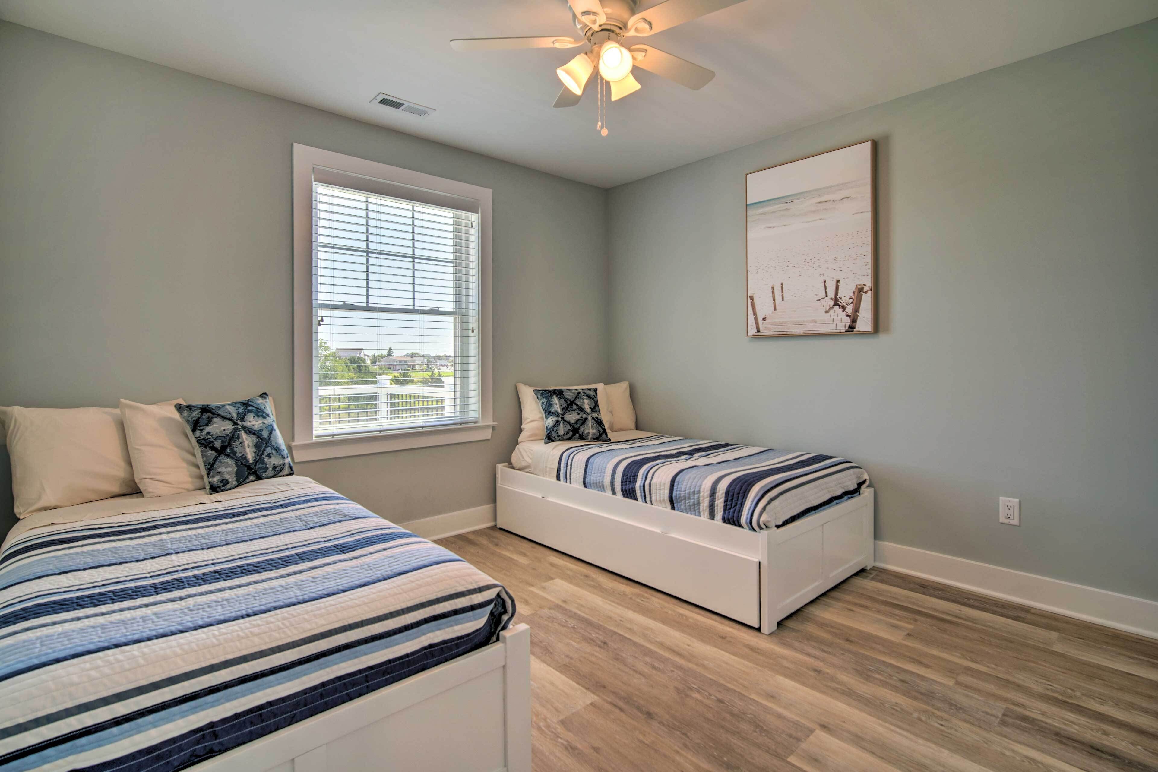 A bedroom with two beds, a ceiling fan, a window with blinds, and a painting on the wall.