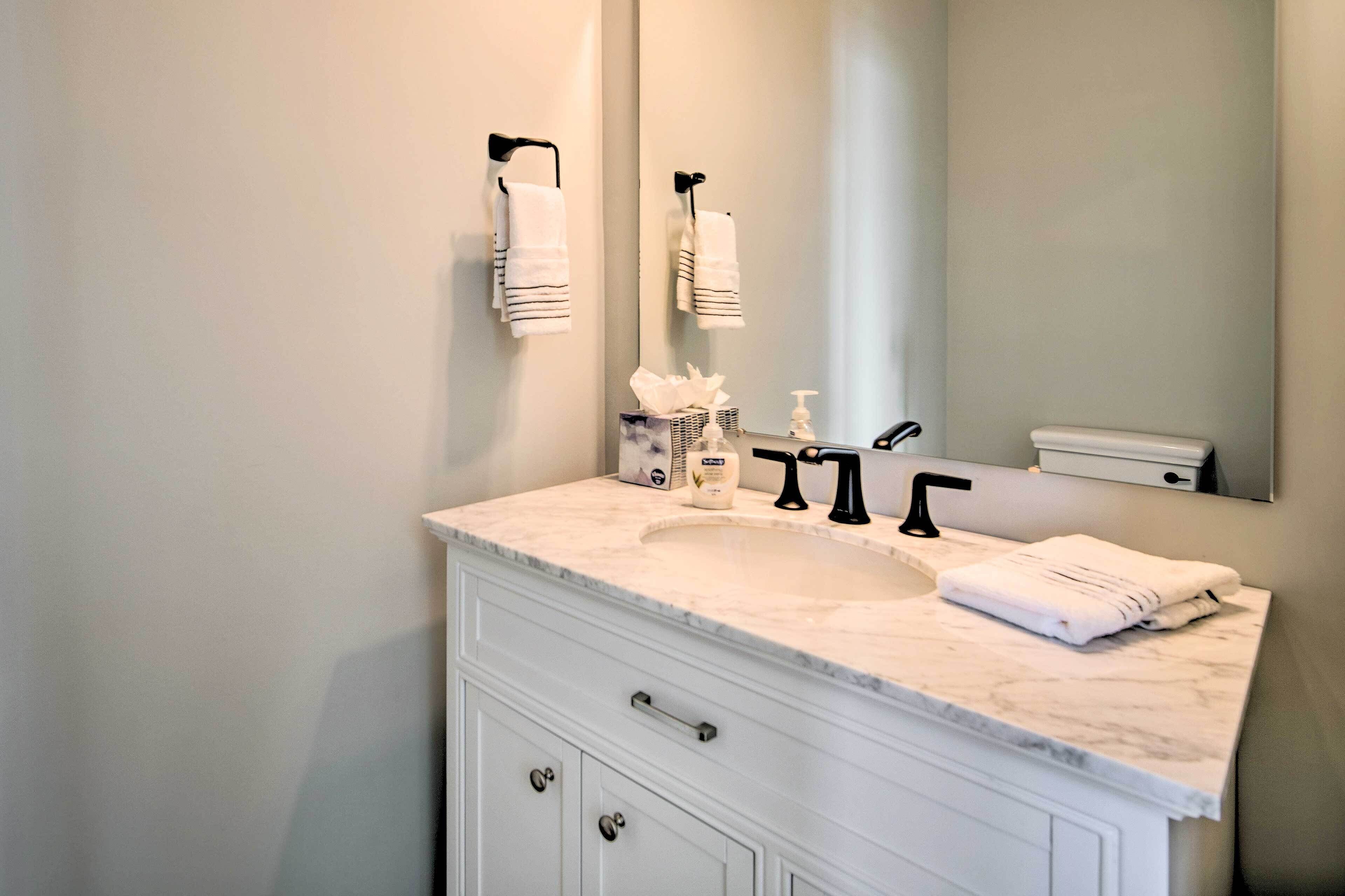 A bathroom with a white marble sink, black faucet, and a large mirror. There are two towels hanging on hooks above the sink.