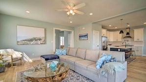 A modern living room with a glass coffee table, a beige sofa with patterned cushions, and a blue patterned rug. - Gorgeous Newly Built Home: Golf Course View! (Brigantine)