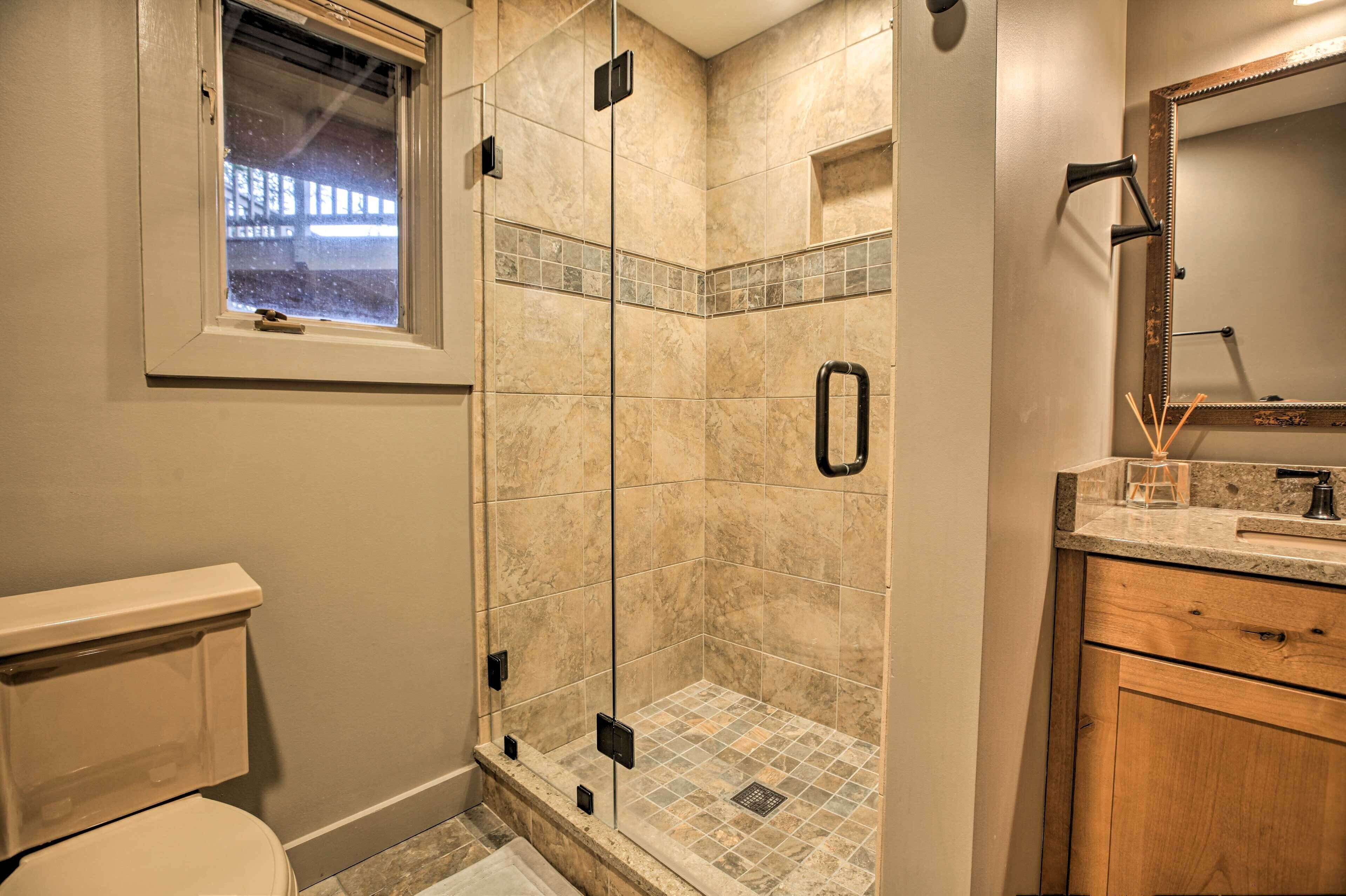 A bathroom with a glass-enclosed shower, a toilet, a sink with a mirror, and a window.