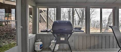A covered outdoor area with a barbecue grill, gas cylinders, and a view of the surrounding landscape.