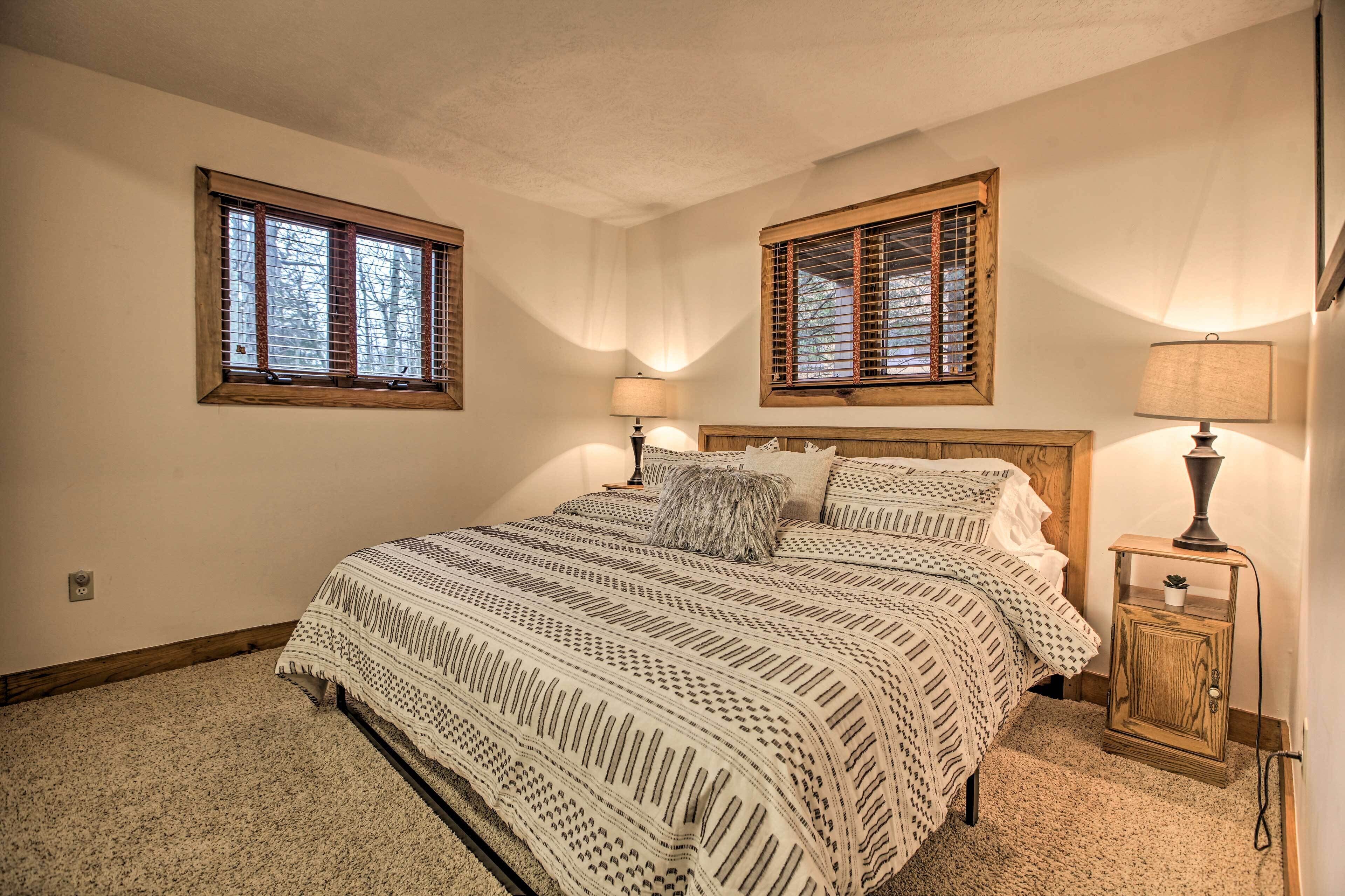 Une chambre à coucher avec un grand lit, deux fenêtres avec des volets en bois, une table de chevet avec une lampe et une petite armoire.