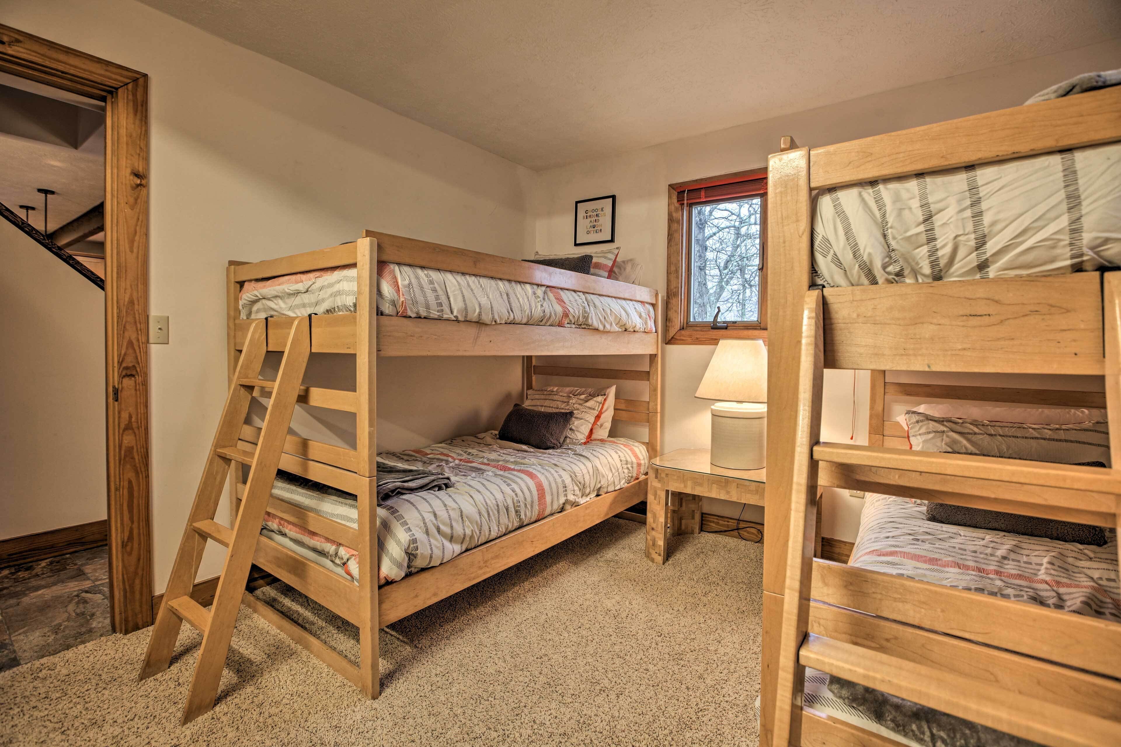 A room with two bunk beds, a wooden ladder, a small table, and a window with a view of trees.