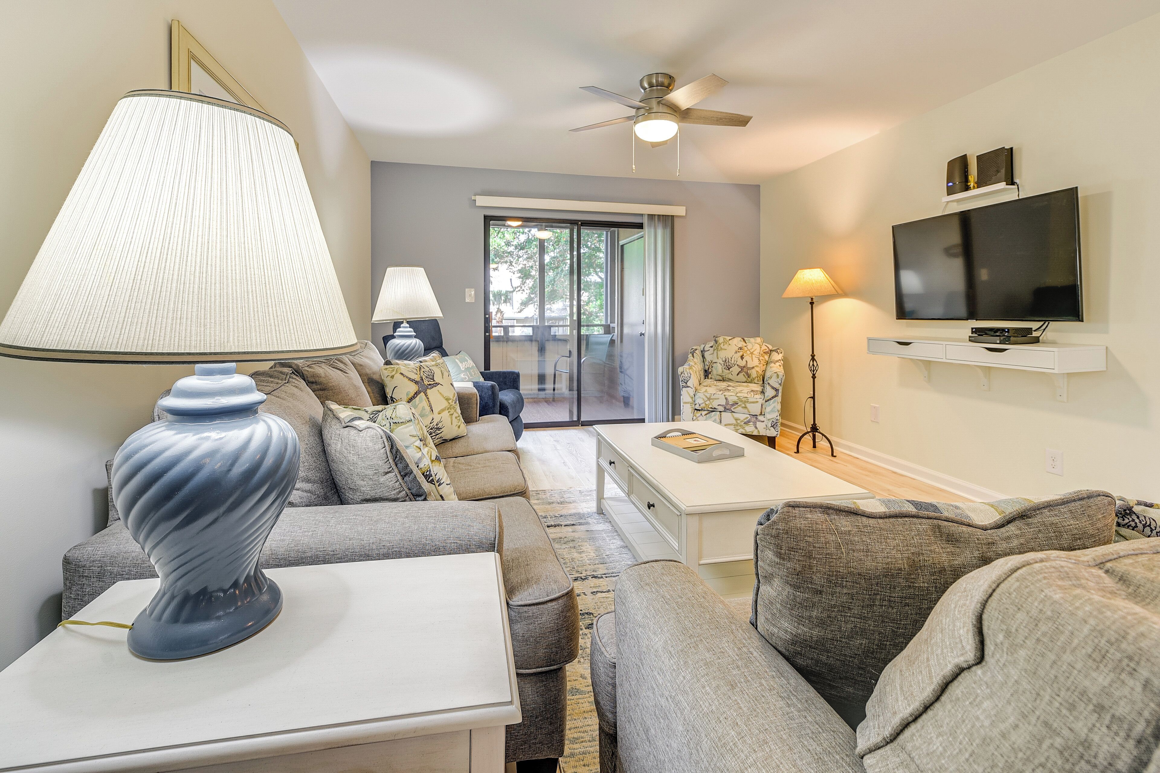 A living room with a sofa set, a coffee table, a lamp, a TV mounted on the wall, and a ceiling fan.