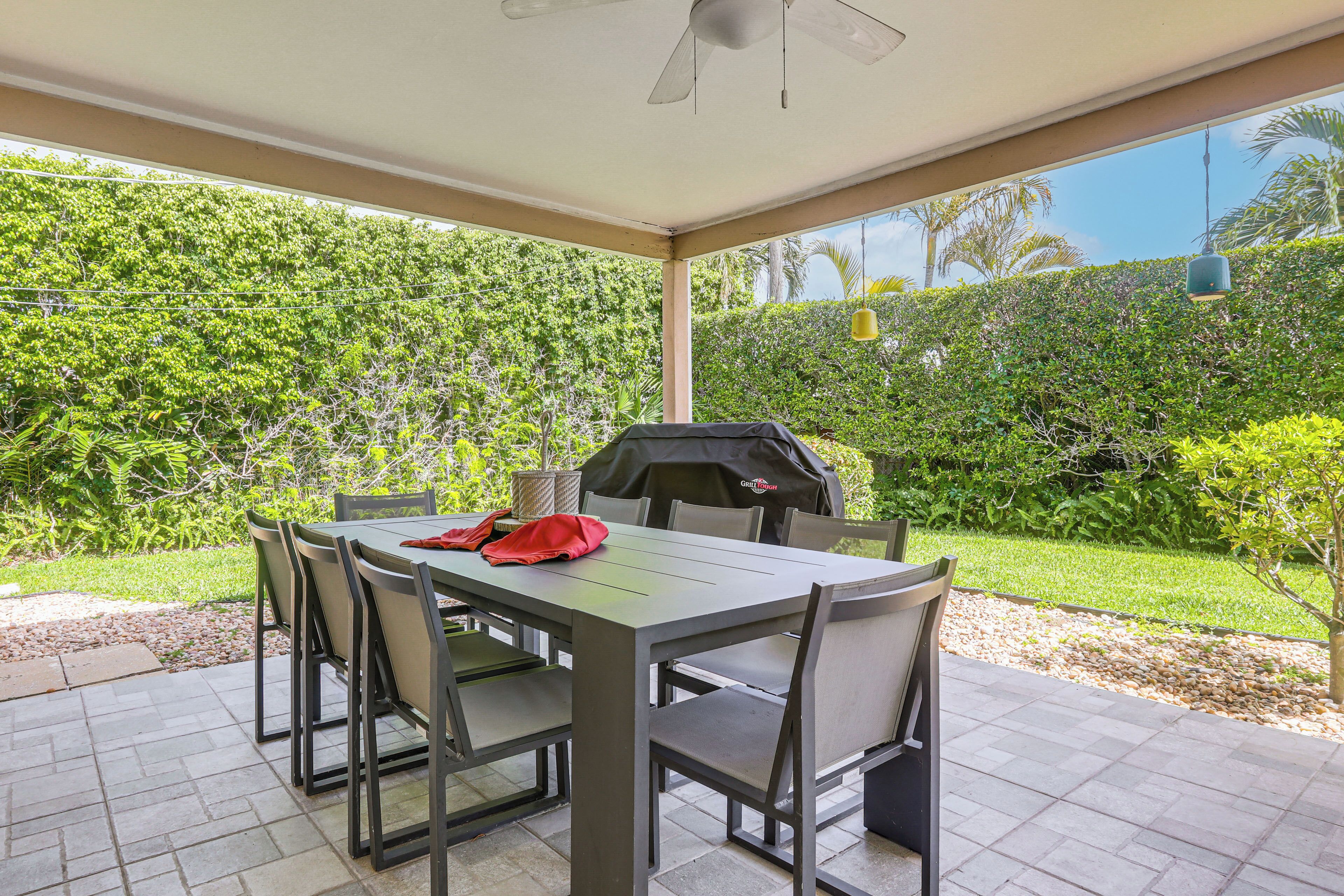 An outdoor patio with a table and chairs, a grill, and a view of a lush garden.