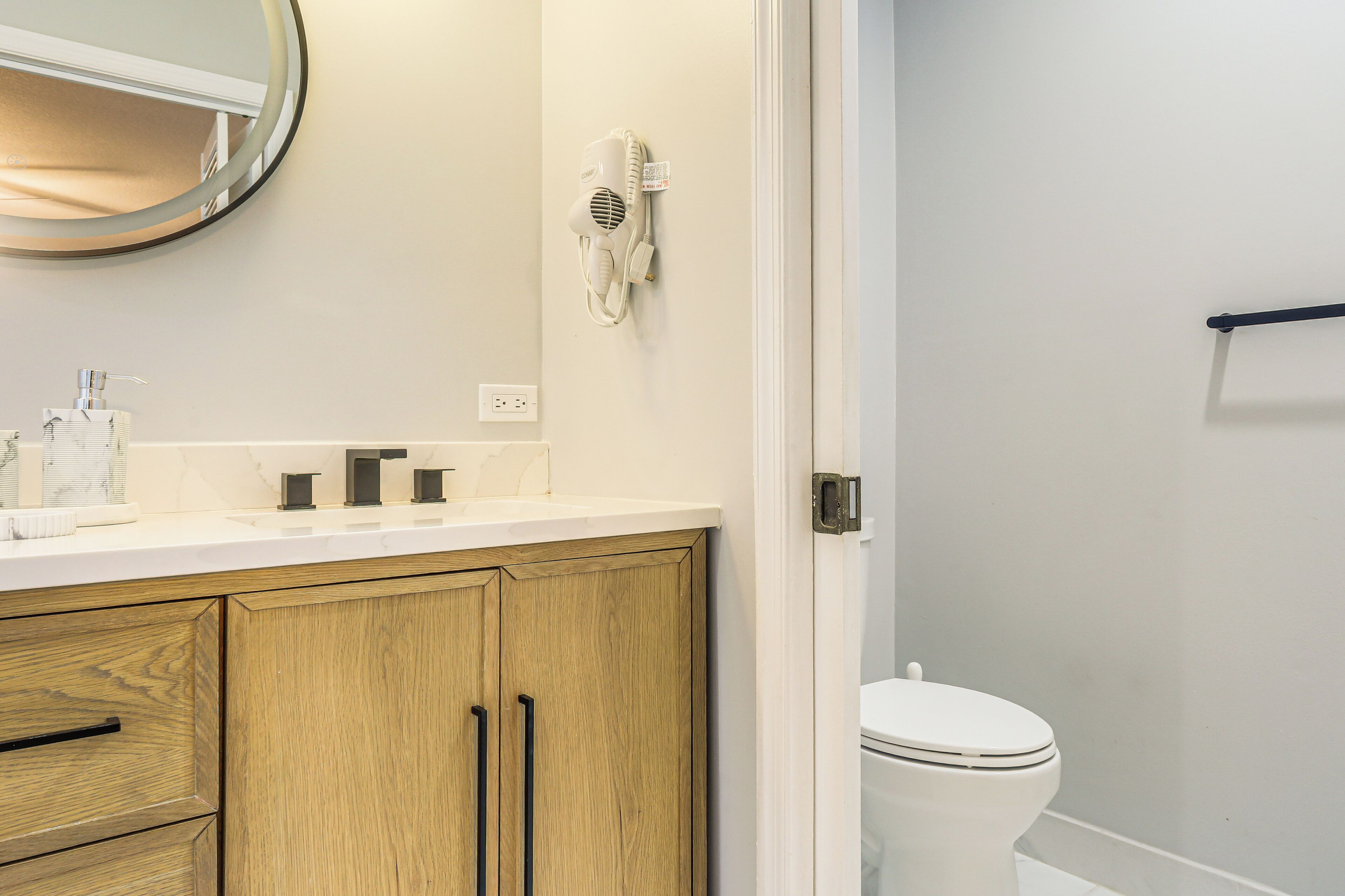 A bathroom with a white sink, wooden cabinets, a hairdryer, and a toilet.