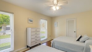 Une chambre avec deux lits, une commode, un ventilateur de plafond et une porte.
