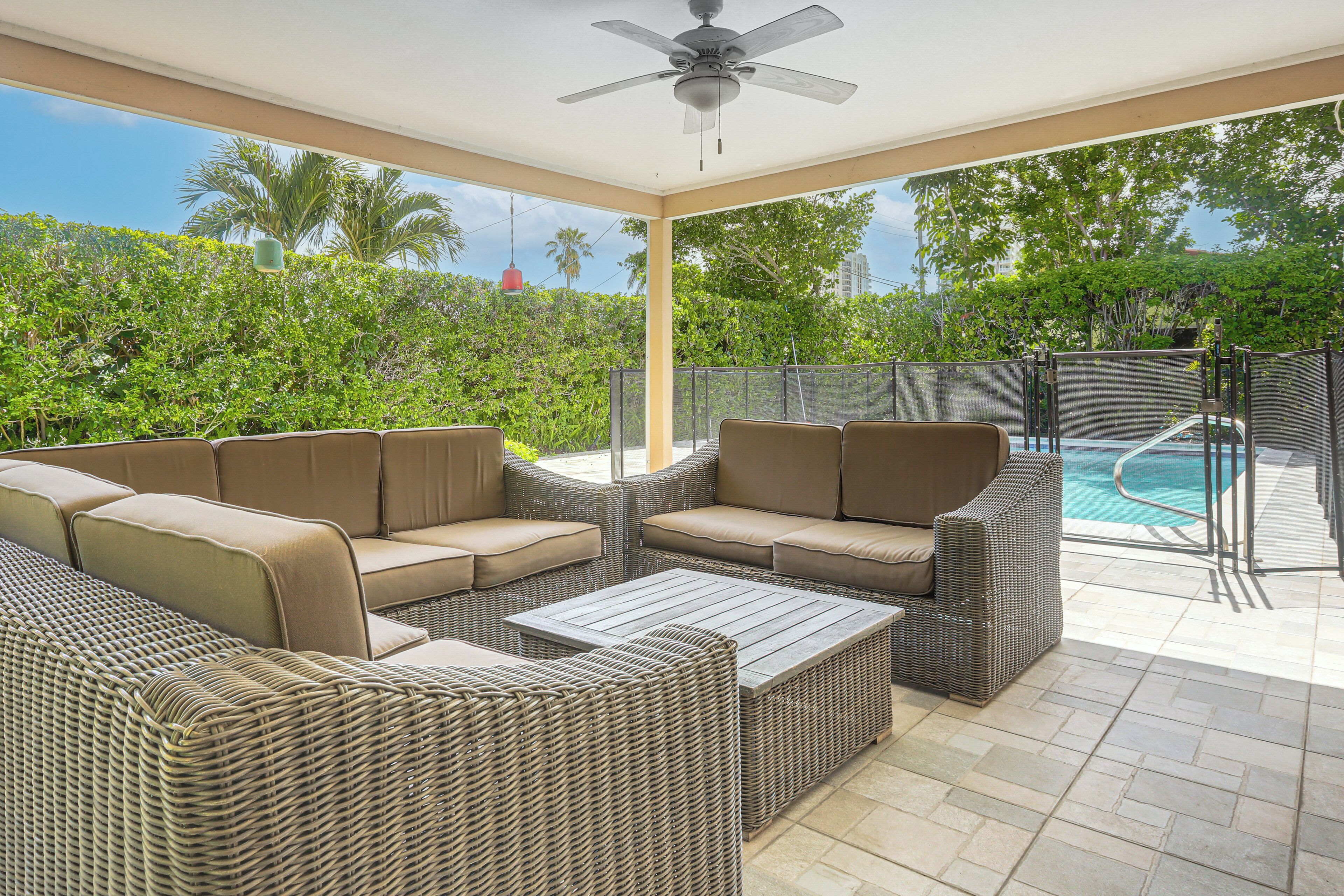 A covered outdoor seating area with wicker furniture and a pool in the background.
