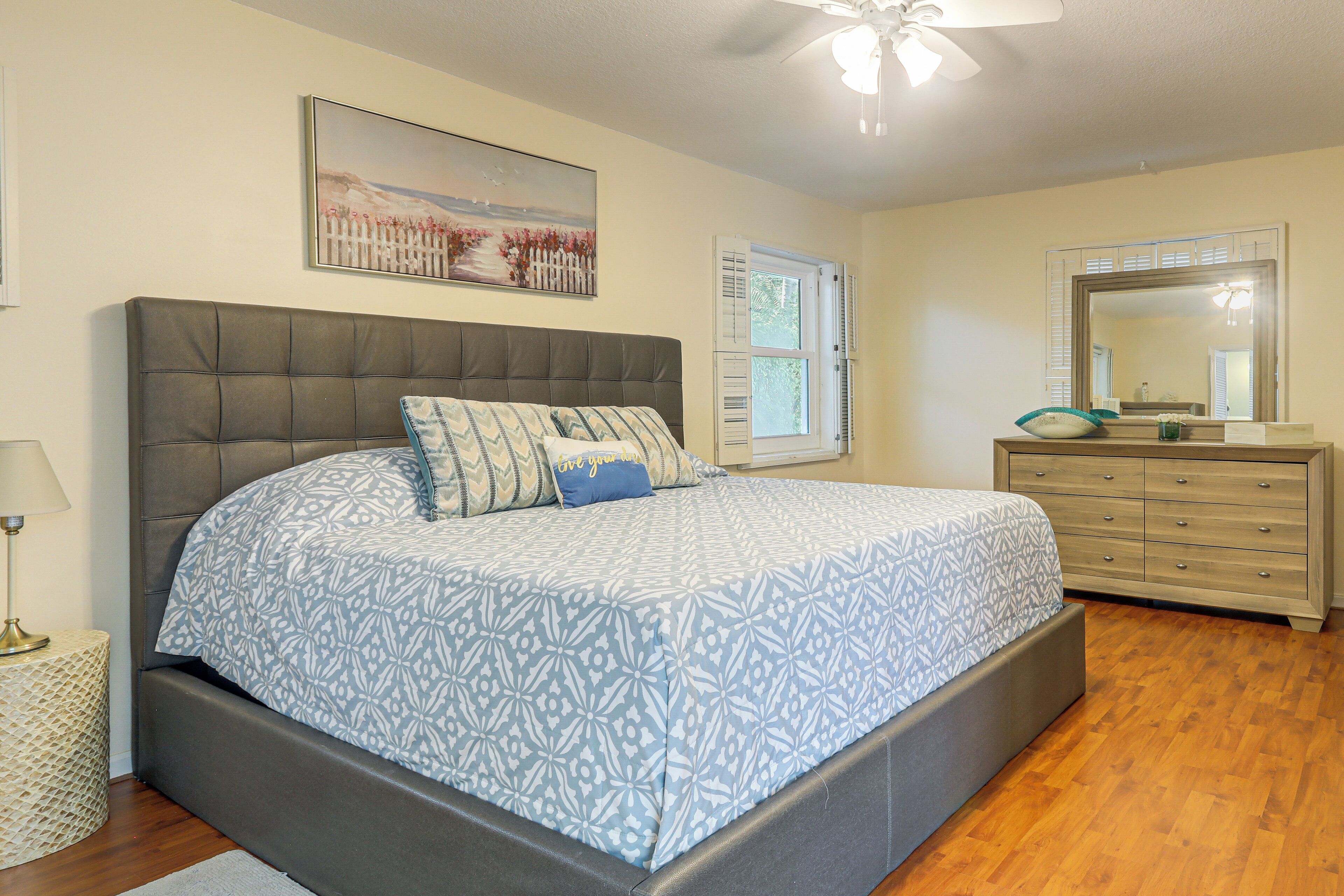 A bedroom with a large bed, a dresser, a mirror, a window with shutters, and a ceiling fan.