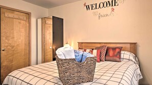 A bedroom with a bed, a welcome sign, a wooden wardrobe, and a hanging basket with towels.