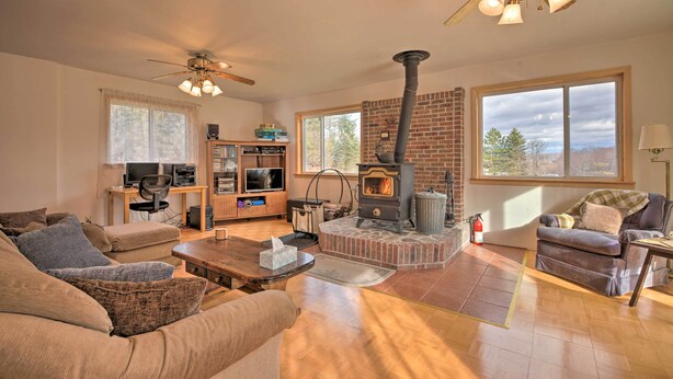 A living room with a fireplace, a ceiling fan, and a large window.