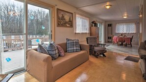 A cozy living room with a sofa, a dining table with chairs, and large windows offering a view of the outdoors.