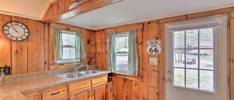A wooden interior with a kitchen area, including a sink, cabinets, and a clock.