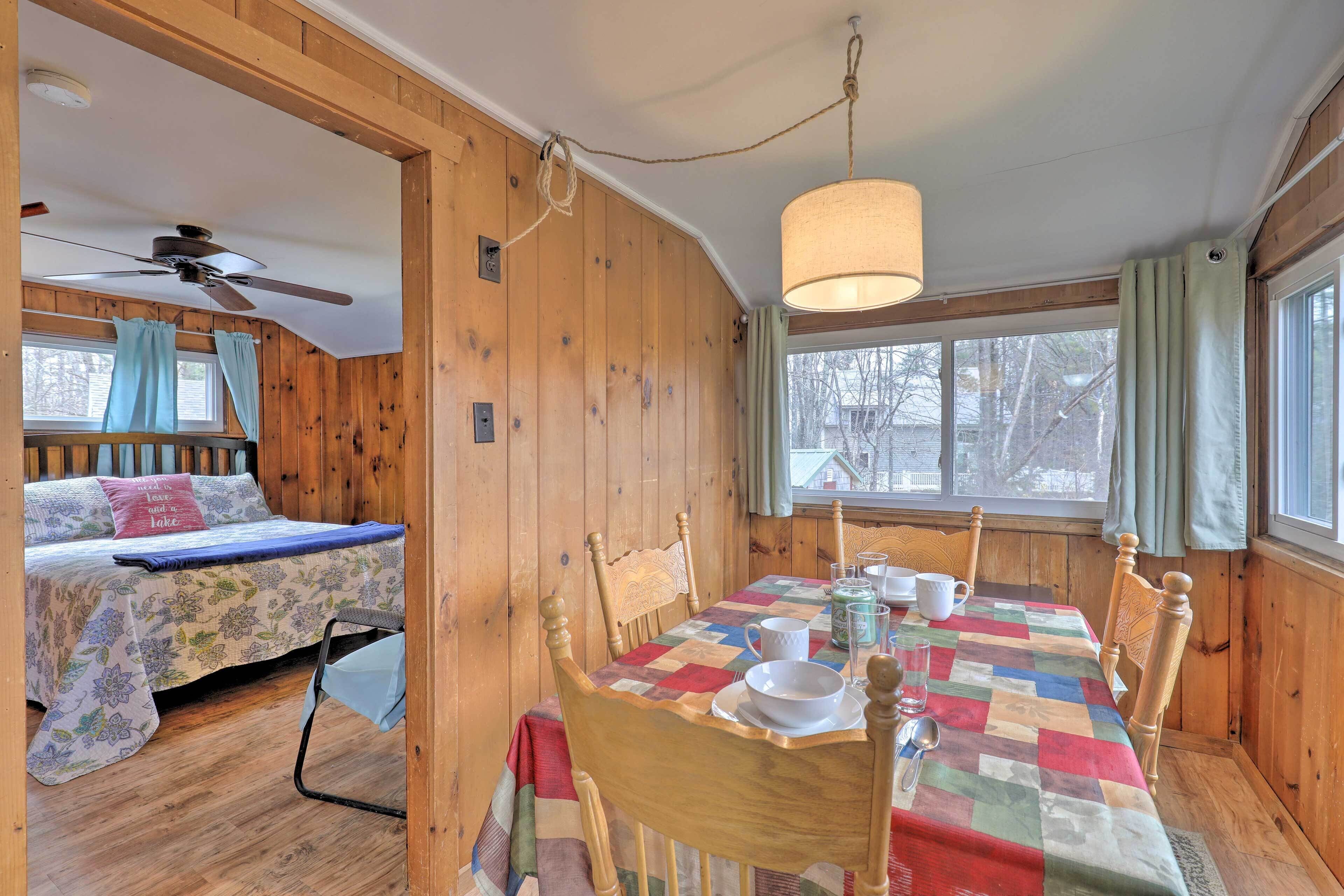 A cozy cabin interior with a wooden interior, a dining table set with plates and cups, and a bed with a floral bedspread.